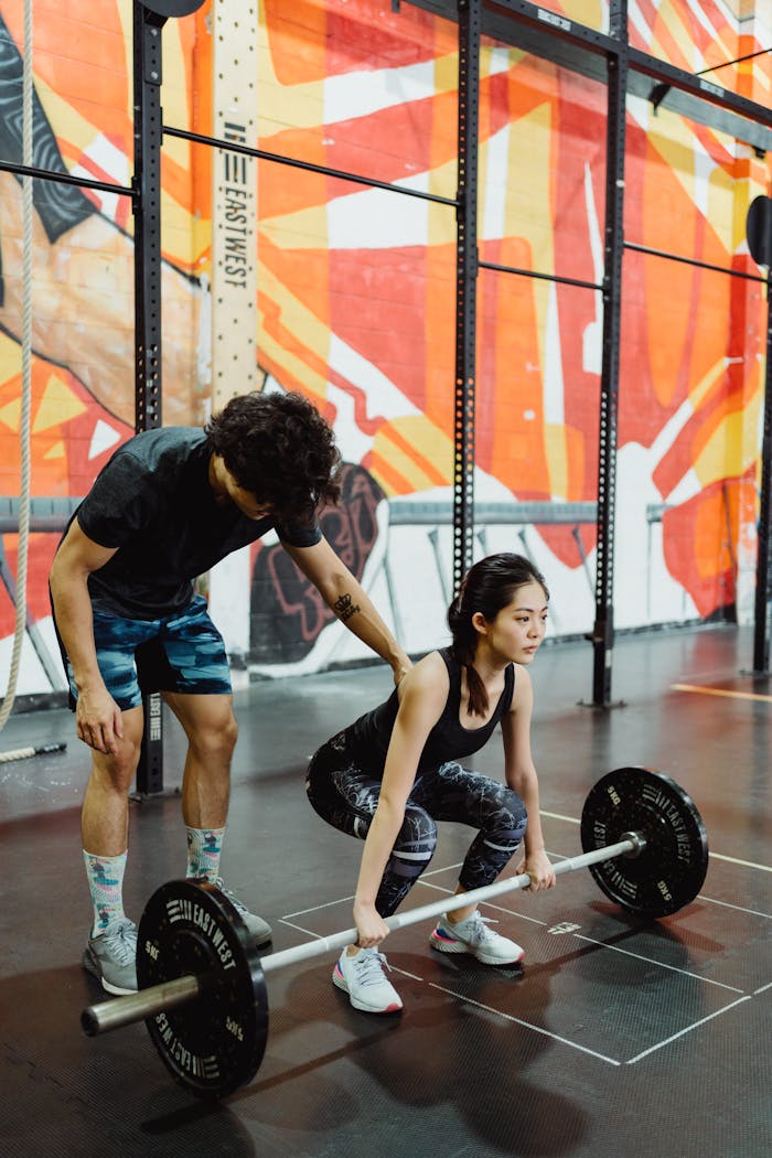 A young woman lifting weights guided by a coach in a colorful indoor gym setting.